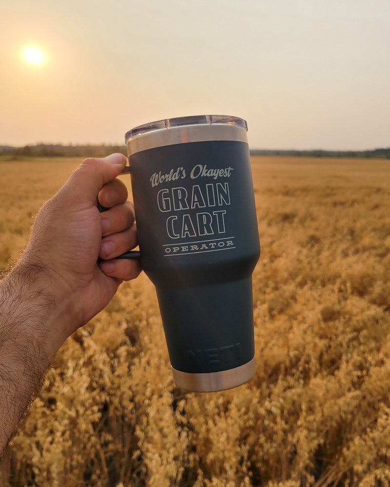 Person holding a tumbler with text in a field at sunset